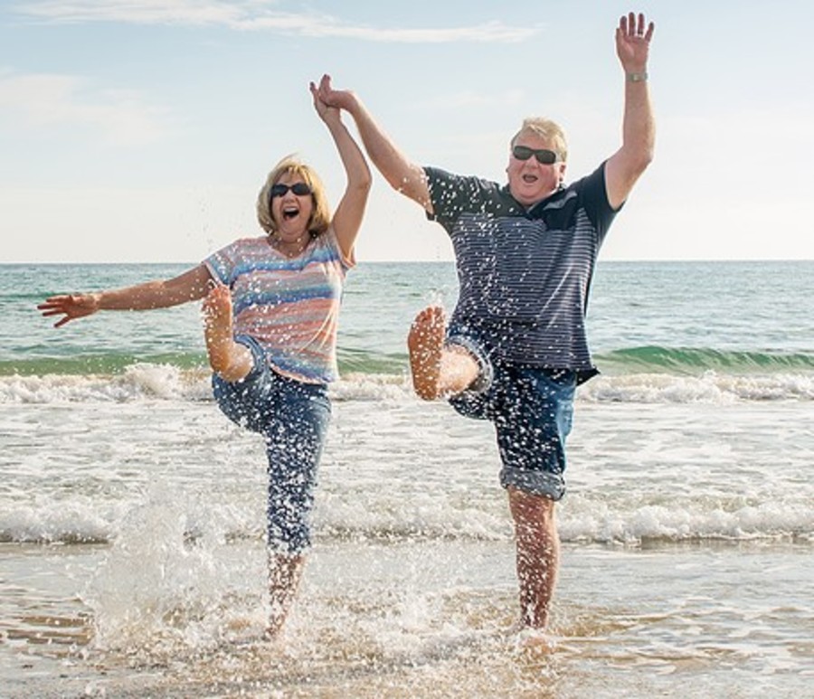 Happy older couple kicking up on the beach.